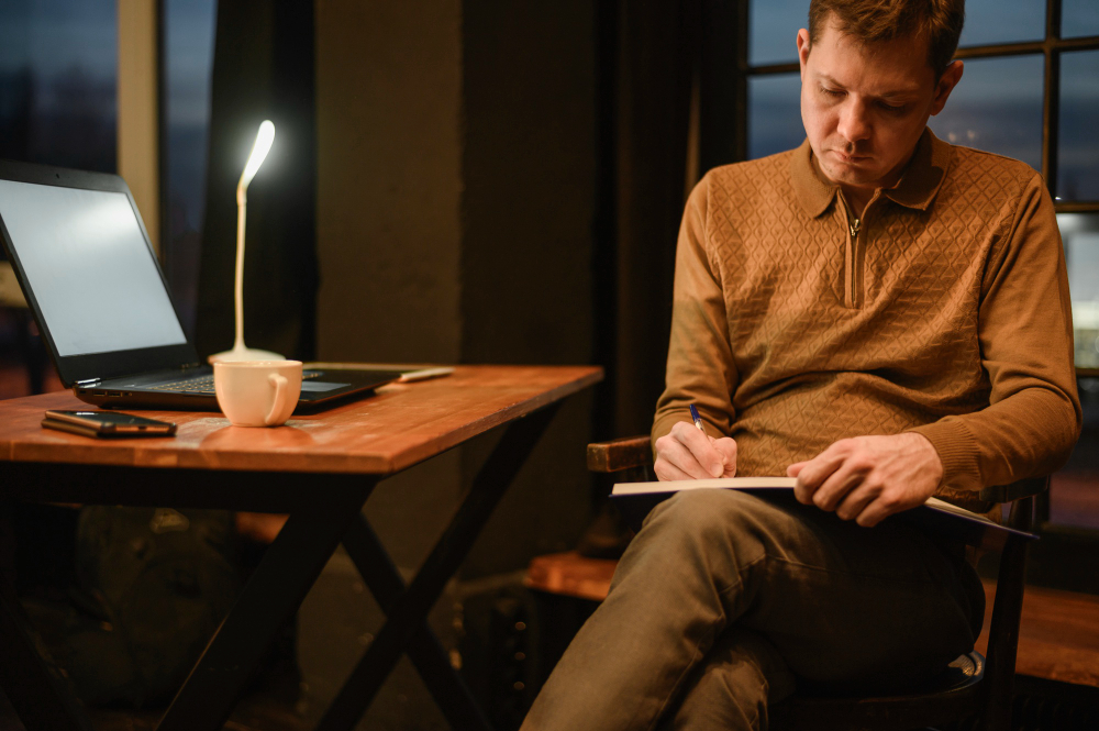 גבר בוגר יושב וכותב במחברת בסביבה שקטה, משקף מאמץ מתמשך ותפקוד יומיומי שדורש השקעה גבוהה